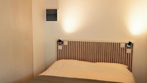 Ein Schlafzimmer mit Holzbalkendecke, einem Bett mit gestreifter Kopfteil und einer kleinen Wandleuchte.