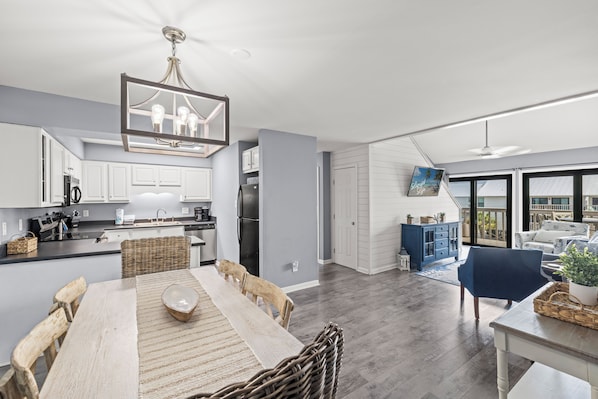 A modern kitchen with white cabinets, a dining area with a wooden table and chairs, and a blue armchair.