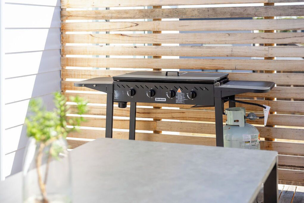 Ein tragbarer Grill mit vier Drehreglern und einer Gasflasche auf einem Tisch.