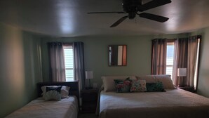 Habitació d'hotel amb dos llits individuals, un ventilador de sostre i una finestra gran amb cortines.