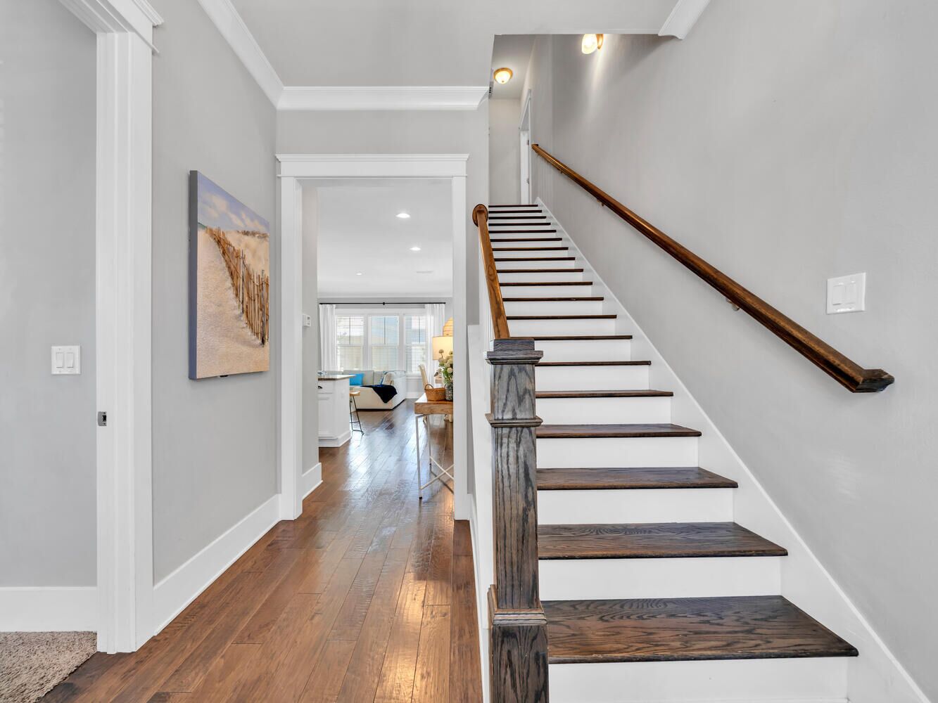 A staircase with wooden steps and a wooden handrail, leading to a room with a white door and a light switch on the wall.