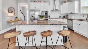 Een moderne keuken met witte kasten, een granieten eiland met barstoelen, roestvrijstalen apparatuur en een centraal eiland met een mand vol fruit.