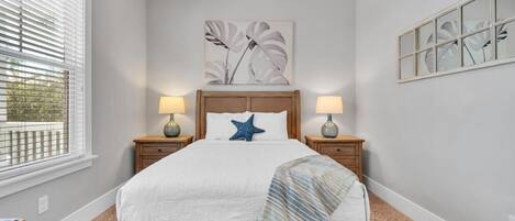 A bedroom with a wooden bed, two bedside lamps, a starfish pillow, and a large window with blinds.