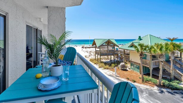 A balcony with a view of the beach, a table with plates and a bottle, and a chair. - 🌊Islander 307 - Once Upon A Tide | Gulf Views-Pool-Beach Service🌊 (Fort Walton Beach)