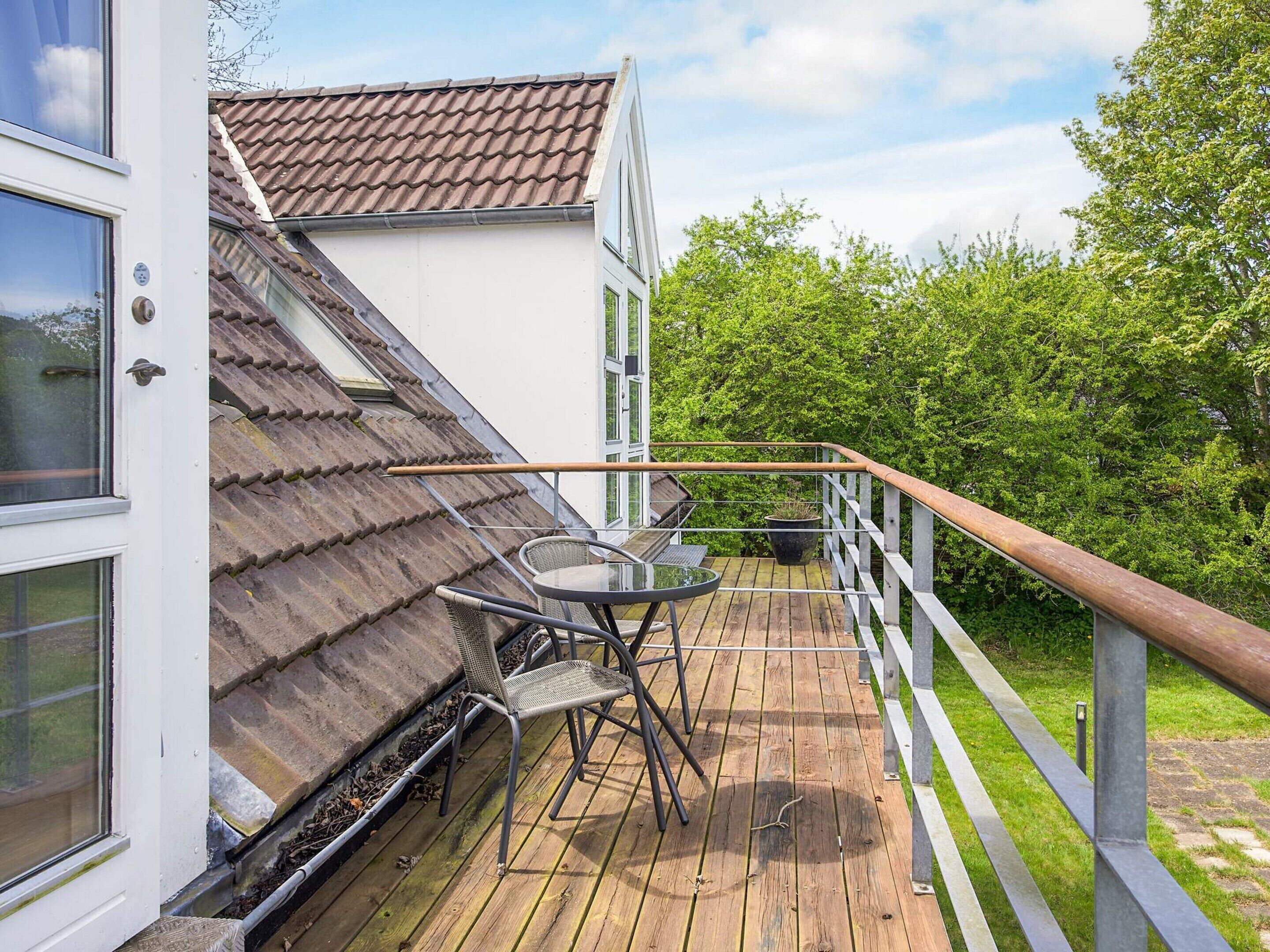 Eine Holzterrasse mit Tisch, Stühlen, Geländer und Blick auf eine grüne Landschaft.