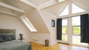 A bedroom with a sloped ceiling, a bed, a nightstand, a lamp, a window, and a door. - 5 Star Holiday Home in Liseleje (Liseleje)