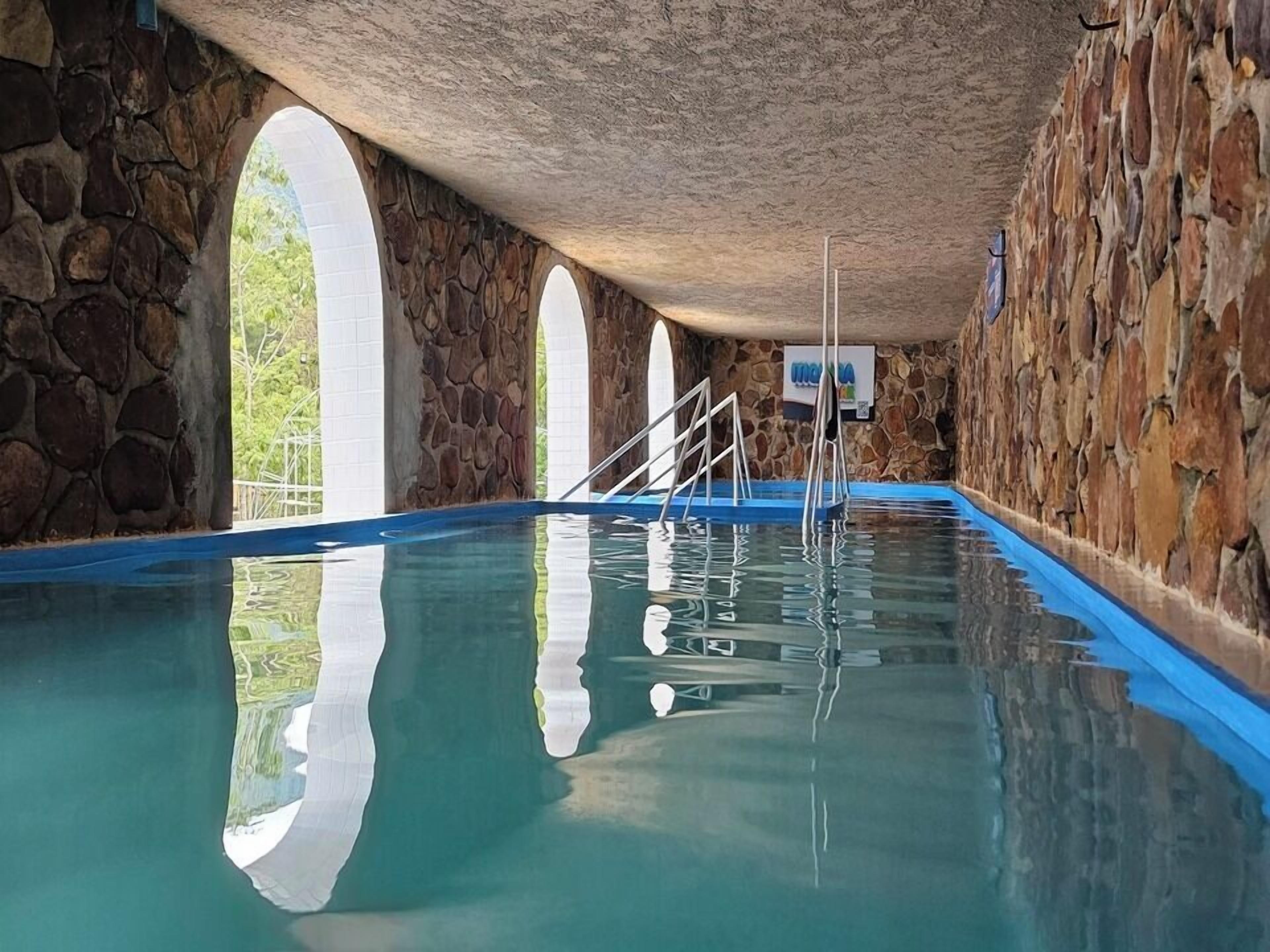 Piscina interior com paredes de pedra e janelas em arco.