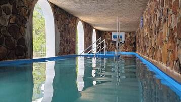 Piscina interior com paredes de pedra e janelas em arco.