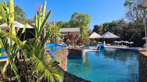 A swimming pool with a stone edge, surrounded by lounge chairs and umbrellas, with tropical plants in the foreground. - Itiquira Park Hotel (Formosa)