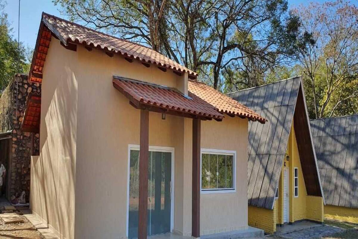 Una casa pequeña de una sola planta con techo de tejas, un porche delantero y un muro de piedra a la izquierda.