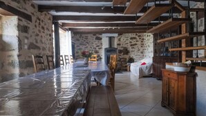 A rustic dining area with a long table covered in plastic, stone walls, wooden beams, and a fireplace. - Les Combes de Testas: Accommodation for 24 people, swimming pool, Aveyron Gorges (Sanvensa)