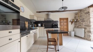 A kitchen with a central island, white cabinets, a stove, and a hanging light fixture. - Les Combes de Testas: Accommodation for 24 people, swimming pool, Aveyron Gorges (Sanvensa)