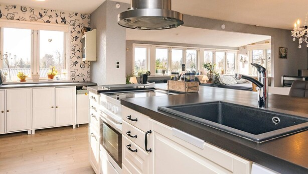 A modern kitchen with white cabinetry, a stainless steel range hood, and a large island with a black countertop and sink. - 4 Person Holiday Home in Vordingborg (Vordingborg)