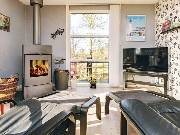 A living room with a wood-burning stove, a television, and a large window with a view of trees and buildings.
