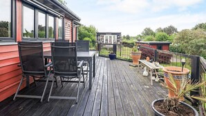 A wooden deck with a table and chairs, potted plants, and a view of a neighboring building. - 4 Person Holiday Home in Vordingborg (Vordingborg)