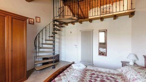 A bedroom with a wooden staircase, a radiator, a bed with a quilt, and a wardrobe. - Casa Rondinella By Case al Lago (Cavriana)