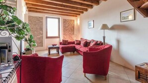 A cozy living room with a red sofa set, a wooden ceiling, and a stone wall. - Casa Rondinella By Case al Lago (Cavriana)