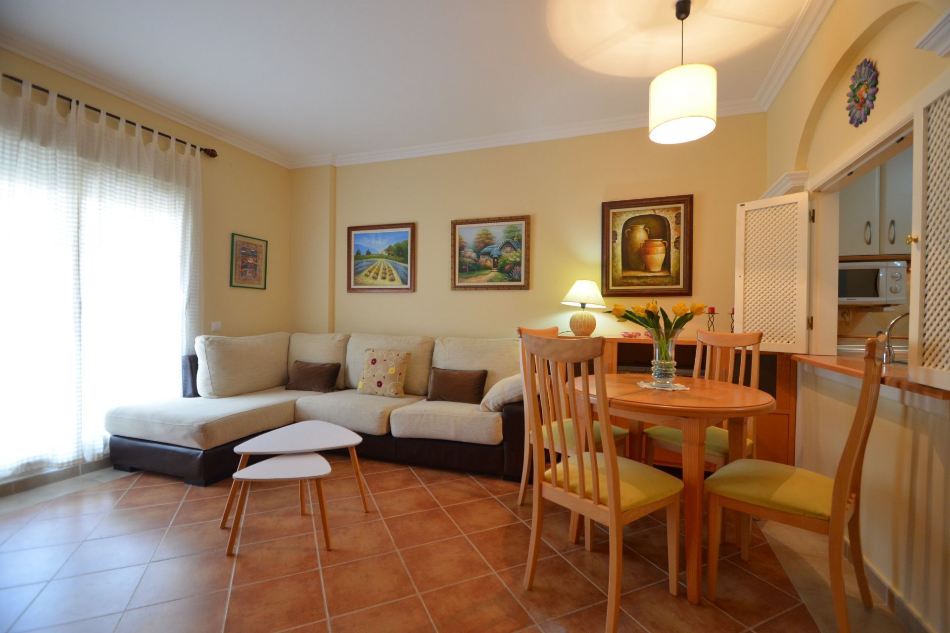 Una sala de estar con un sofá, una mesa de comedor con sillas y una zona de cocina con microondas.