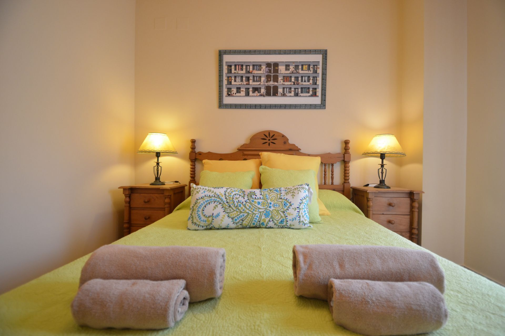 A neatly made bed with two pillows, two bedside tables with lamps, and a framed picture on the wall.