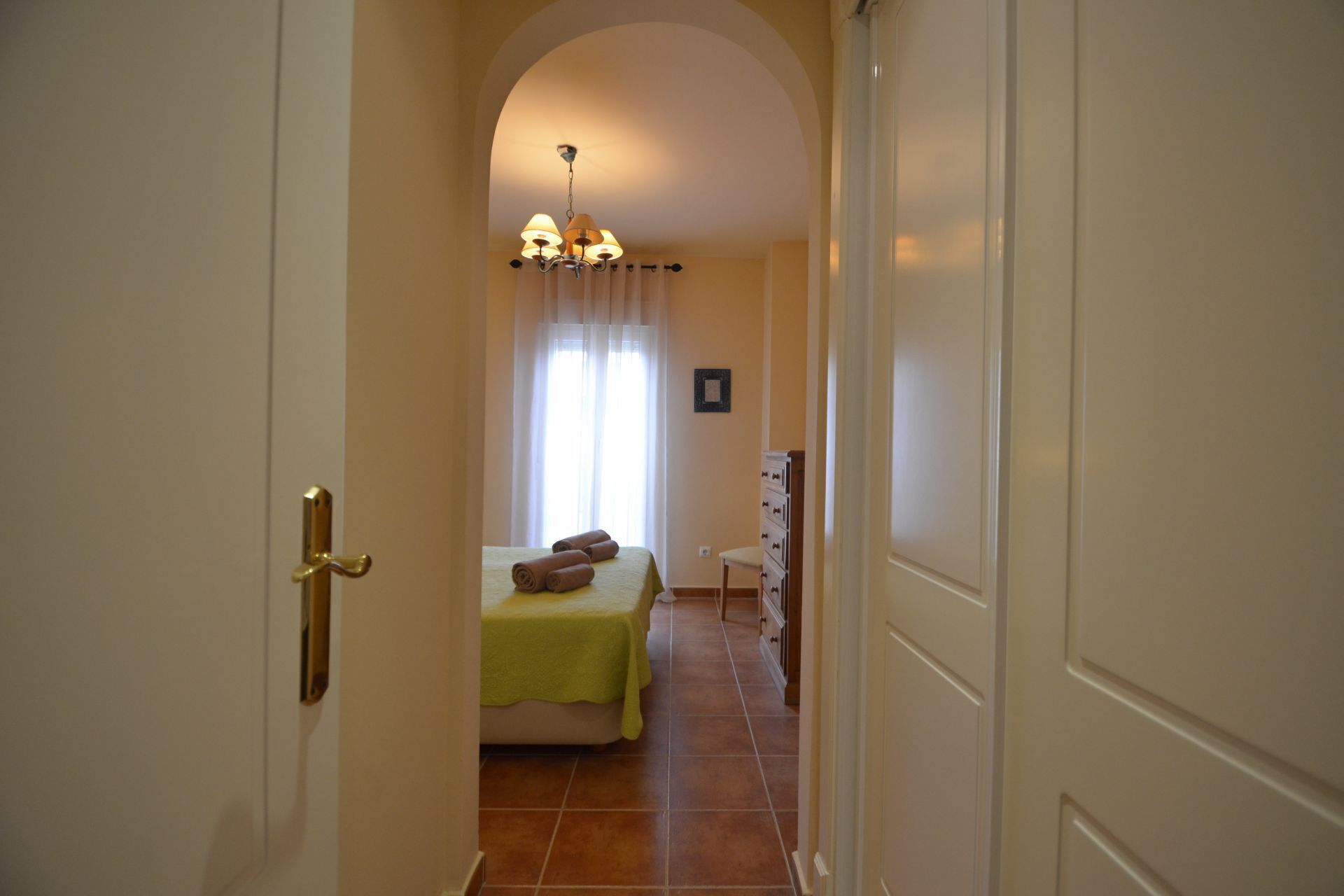 A hallway leading to a bedroom with a bed, a dresser, and a chandelier.