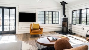 Un salón moderno con chimenea, un sillón de cuero, una mesa de centro redonda y ventanas amplias.