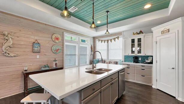 Una cocina con una isla central, armarios blancos, techo color turquesa y decoración en las paredes.
