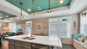 Una cocina con una isla central, electrodomésticos de acero inoxidable y un techo color esmeralda.
