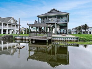 A waterfront house with a balcony, a dock, and a reflection in the water.
