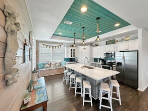 A modern kitchen with a central island, white cabinetry, and a teal ceiling.