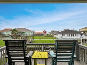 A wooden deck with two chairs and a small table, overlooking a grassy area with houses in the background.