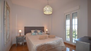 A bedroom with a large bed, two bedside tables with lamps, a hanging light fixture, and a view through a window with a balcony. - San Bruno 73 - Two Bedroom Apartment, Sleeps 5 (Punta del moral)