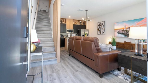 Una sala moderna con un sofá de cuero marrón, una mesa de comedor y una escalera que lleva a una zona de cocina.