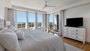 Un dormitorio amplio con una cama grande, un televisor sobre un aparador y un balcón con vista al océano.