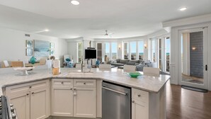 Una cocina amplia con una isla grande, armarios blancos y vista a la playa.