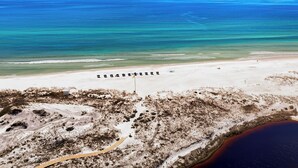 Vista aérea de una playa con una fila de sombrillas y un sendero arenoso que lleva al agua.