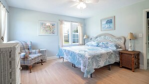 A bedroom with a bed, a chair, a lamp, and a ceiling fan. - Coastal Comfort, Almost Oceanfront Duplex in Salter Path, NC! (Salter Path)