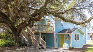 A two-story house with a wooden staircase leading to a balcony, surrounded by large trees. - Coastal Comfort, Almost Oceanfront Duplex in Salter Path, NC! (Salter Path)