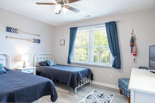 A bedroom with two beds, a ceiling fan, a window with curtains, and nautical-themed decor.