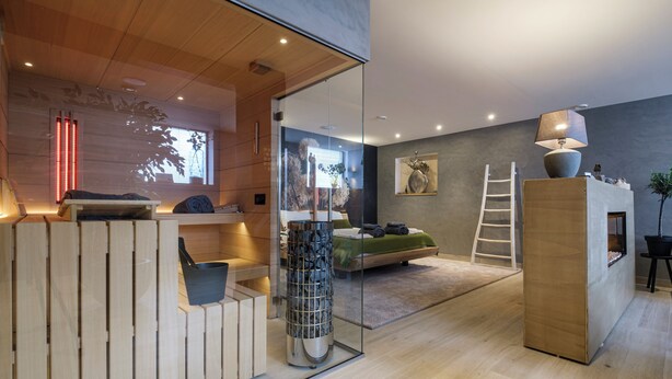 A modern interior with a wooden reception desk, a glass partition, a bed, a ladder, and a fireplace. - Relax in Wellness Room with Sauna and Spa Bath and luxurious outdoor seating. (Nieuwe Niedorp)