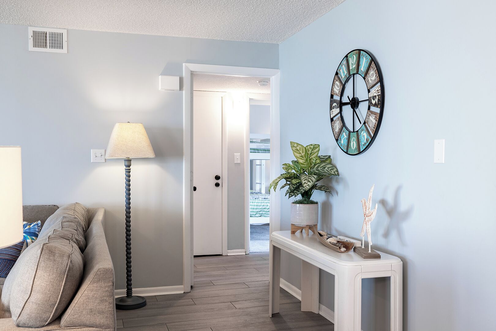 Un salon comprenant un canapé, une lampe, une console sur laquelle est posée une plante, et une horloge murale.