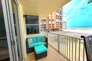 Un balcone con una divanetto e dei cuscini, vista sulla spiaggia e un grattacielo sullo sfondo.