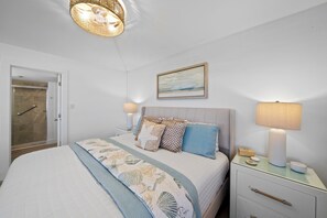 A bedroom with a bed, bedside tables, a nightstand, a shower, and a painting on the wall.