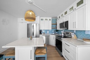 A modern kitchen with white cabinetry, a central island, a stainless steel refrigerator, a microwave, and an oven.