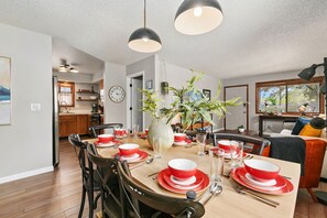 A dining area with a wooden table set for four, surrounded by chairs. A vase with plants is on the table.