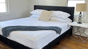 A neatly made bed with white linens and a grey knitted throw, a black upholstered headboard, and a bedside table with a lamp. - Charming 2-bedroom apartment in Saint Paul. Near MAC, UST, St. Kate's. (Saint Paul)