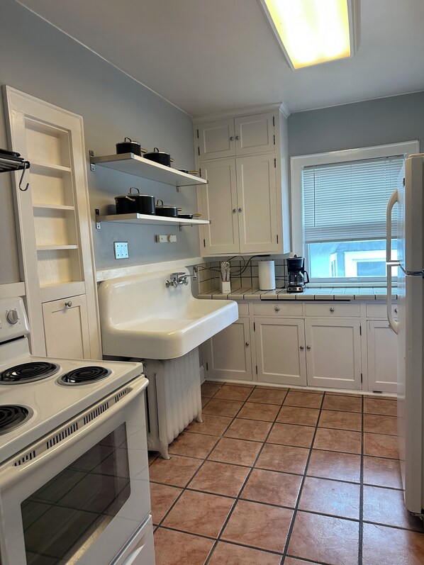 A kitchen with white cabinets, a white sink, a stove, and a window with blinds. - Mac-Groveland • 2 King Beds • Walkable • WiFi • Laundry • Pets welcome! (Saint Paul)