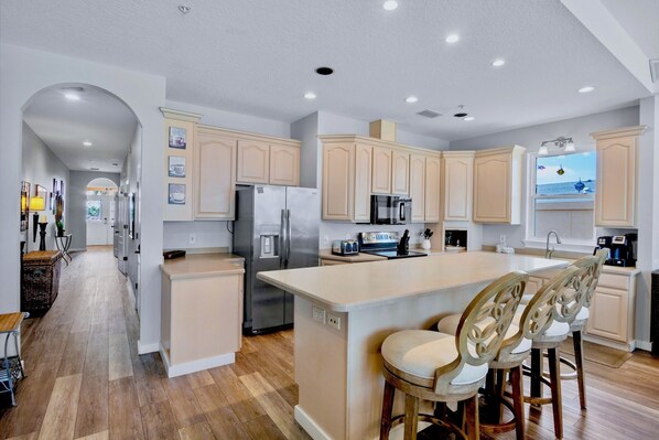 A modern kitchen with a central island, stainless steel appliances, and light wood cabinetry.