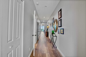 A hallway with white doors, wooden flooring, and framed pictures on the walls.