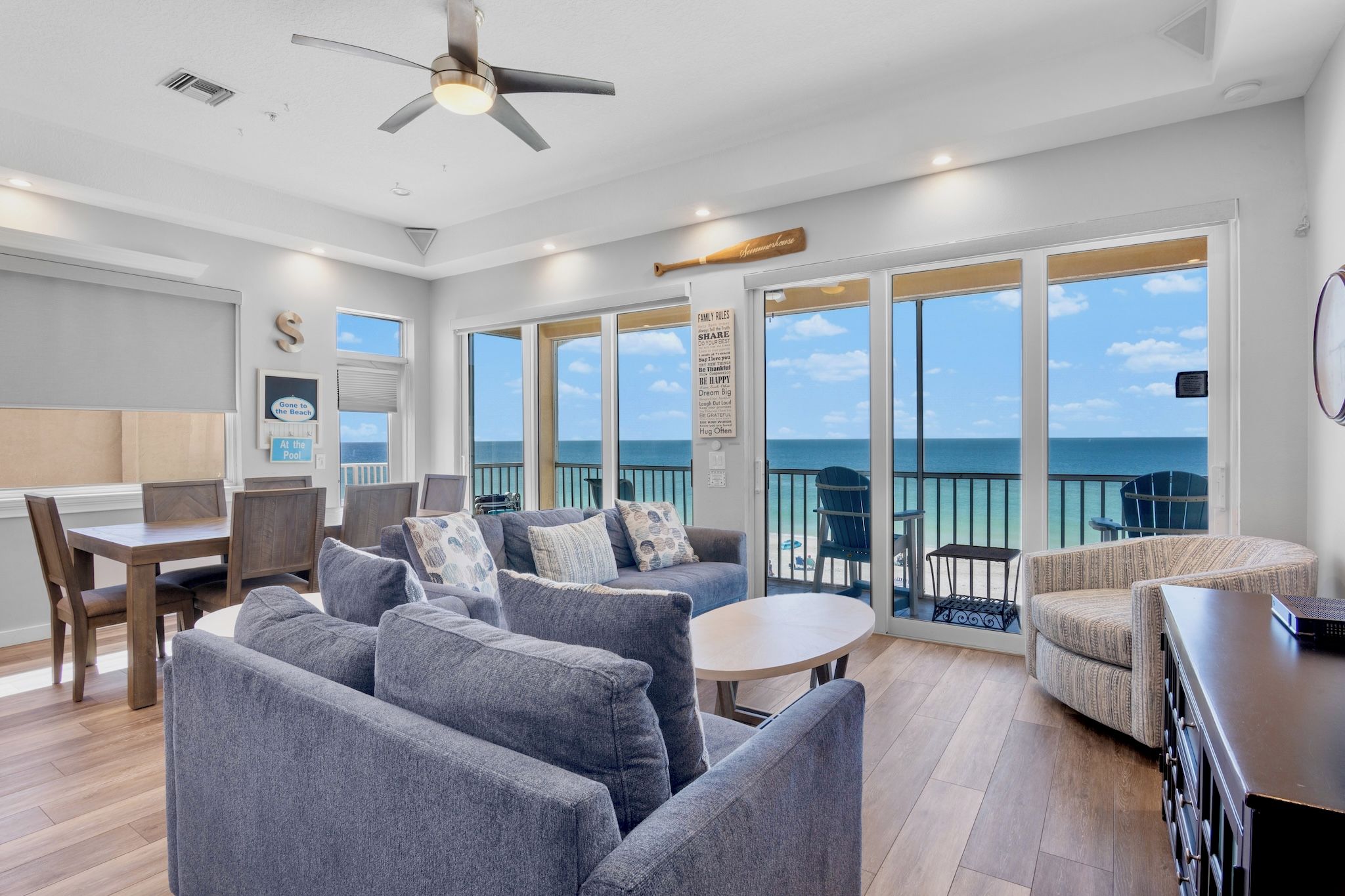 Een ruime woonkamer met een balkon met uitzicht op zee, een eettafel en een plafondventilator.