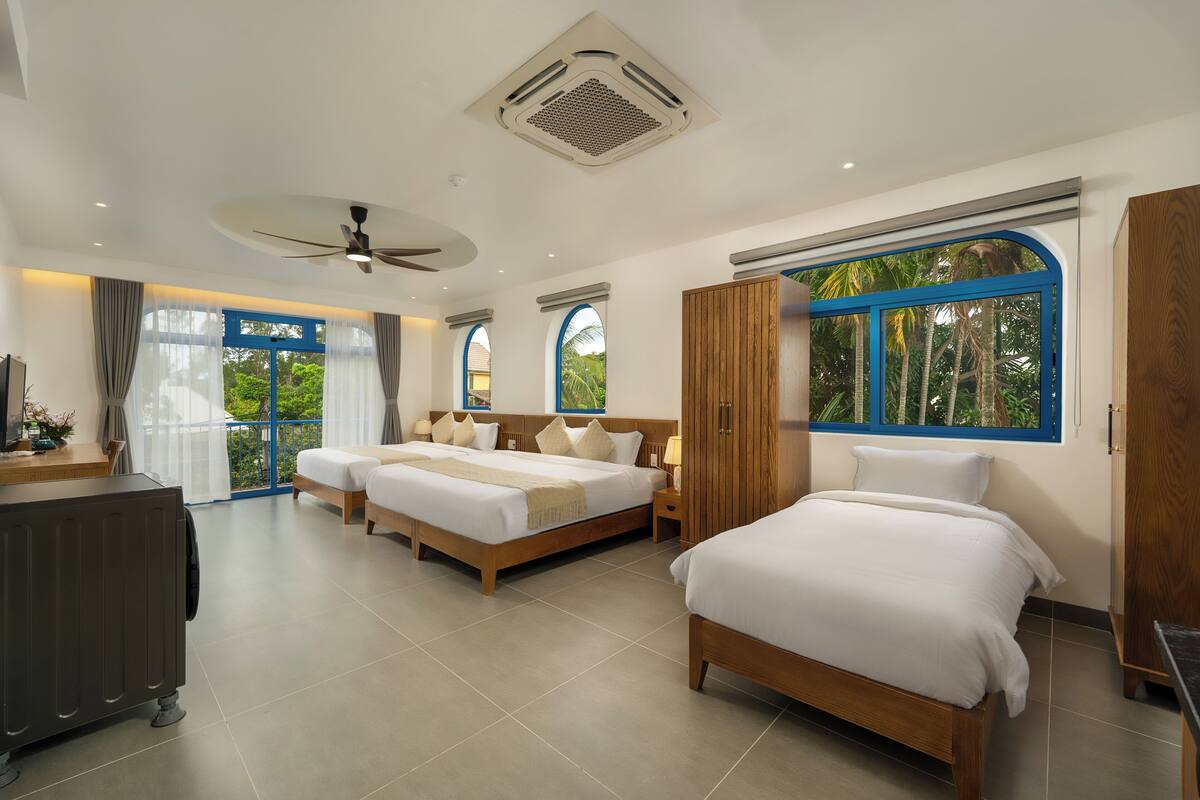 A hotel room with two beds, a ceiling fan, large windows, and a view of greenery.